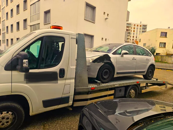 Citroën C4 à l’aile avant endommagée sur un camion entre des immeubles.