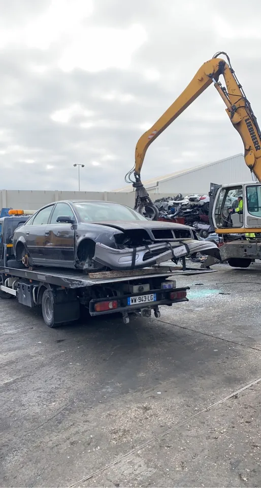 Berline incomplète sans roues posée sur un plateau près d’un engin de manutention.