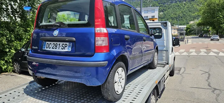 Fiat Panda aux portières enfoncées sur le plateau d’un camion blanc.