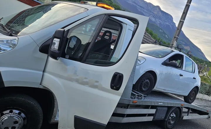 Nissan Micra chargée derrière la cabine d’un camion-plateau blanc.
