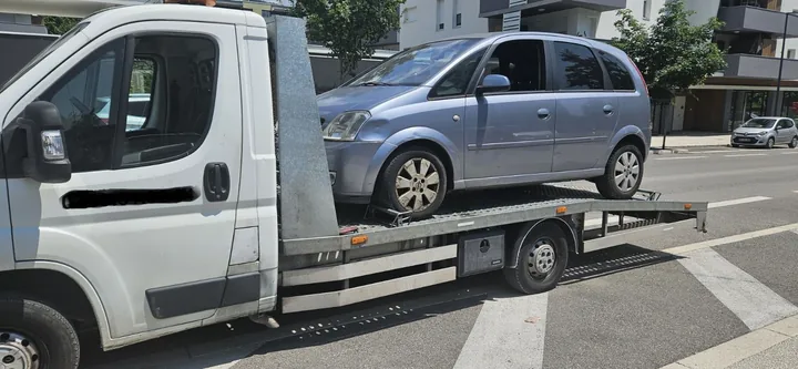 Monospace compact sur une dépanneuse blanche dans une rue bordée d’immeubles.