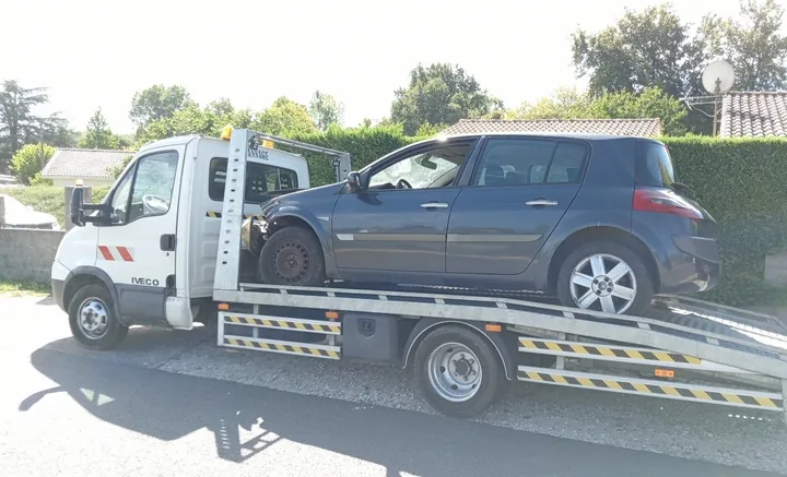 Voiture grise à cinq portes vue de côté sur un camion-plateau blanc.
