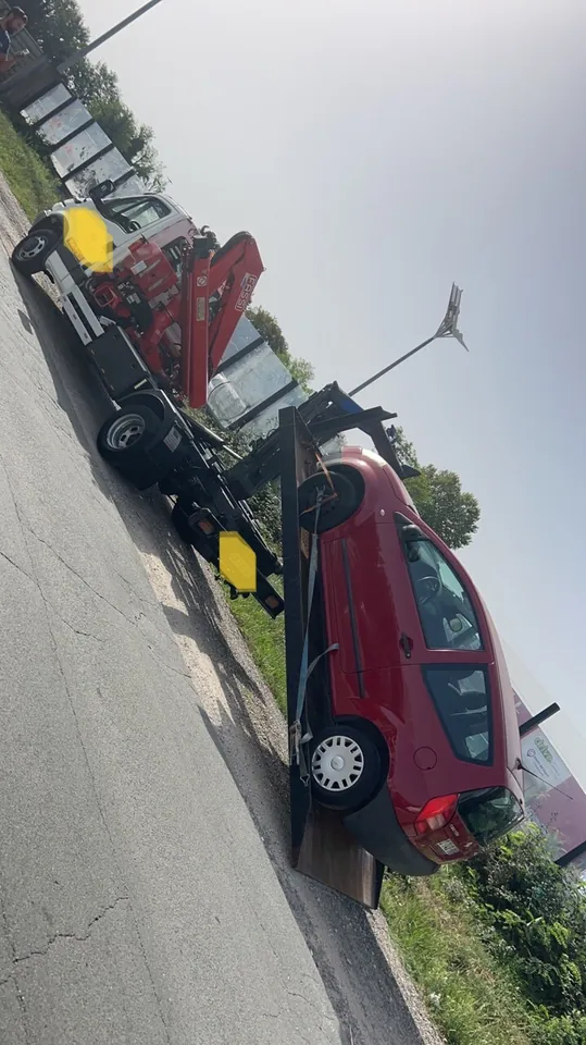 Voiture rouge photographiée de biais sur un camion équipé d’une grue.