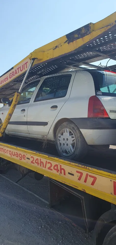 Voiture grise installée sur un camion-plateau portant des inscriptions commerciales.
