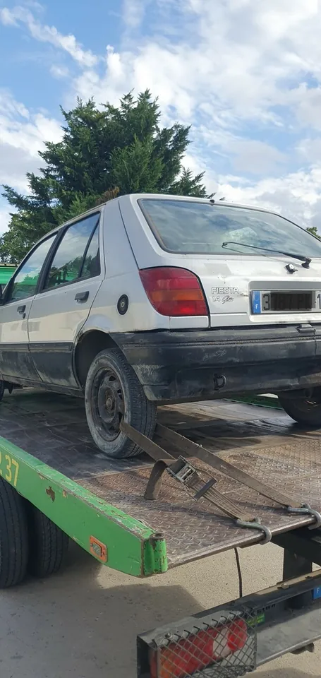 Voiture blanche photographiée sur le plateau d’un camion vert.