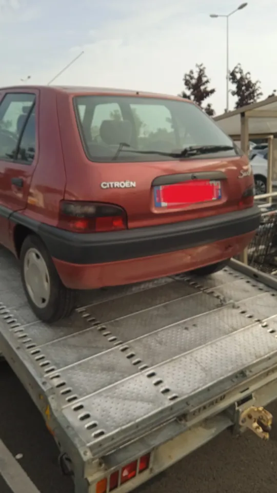 Arrière d’une voiture rouge photographiée sur un plateau de transport.