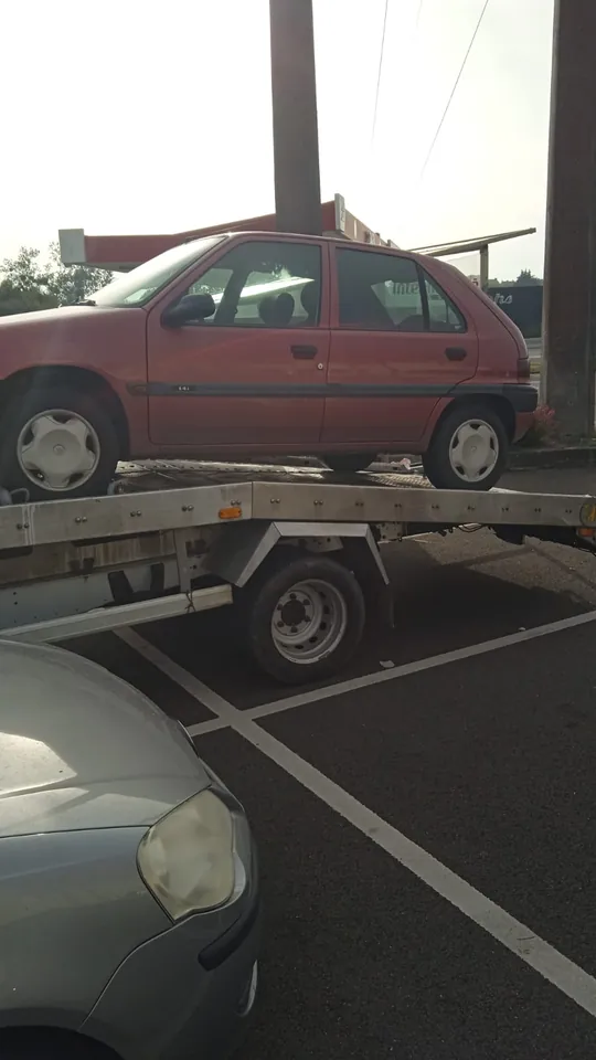 Peugeot 106 chargée sur une dépanneuse entre des places de parking.