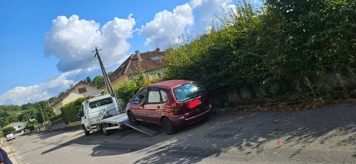 Camion plateau avec ses rampes déployées près d’une voiture rouge.