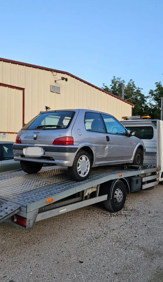 Voiture grise vue de l’arrière sur un camion-plateau devant un bâtiment.