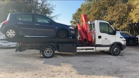 Citadine sombre sur le plateau d’un camion blanc équipé d’une grue rouge.