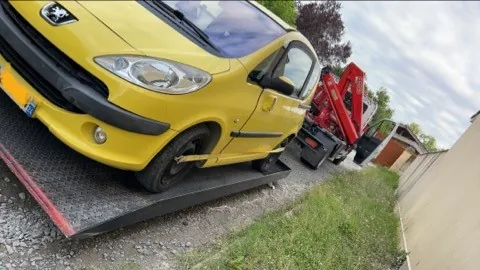 Petite voiture jaune avec une partie avant endommagée, installée sur un plateau.