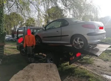 Coupé gris chargé sur un plateau près d’une personne en tenue orange.