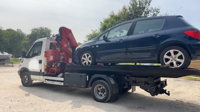 Voiture sombre de profil sur le plateau d’un camion blanc équipé d’une grue rouge.
