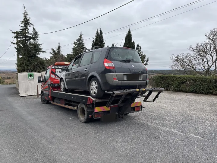 Monospace gris chargé sur un camion équipé d’une grue rouge.