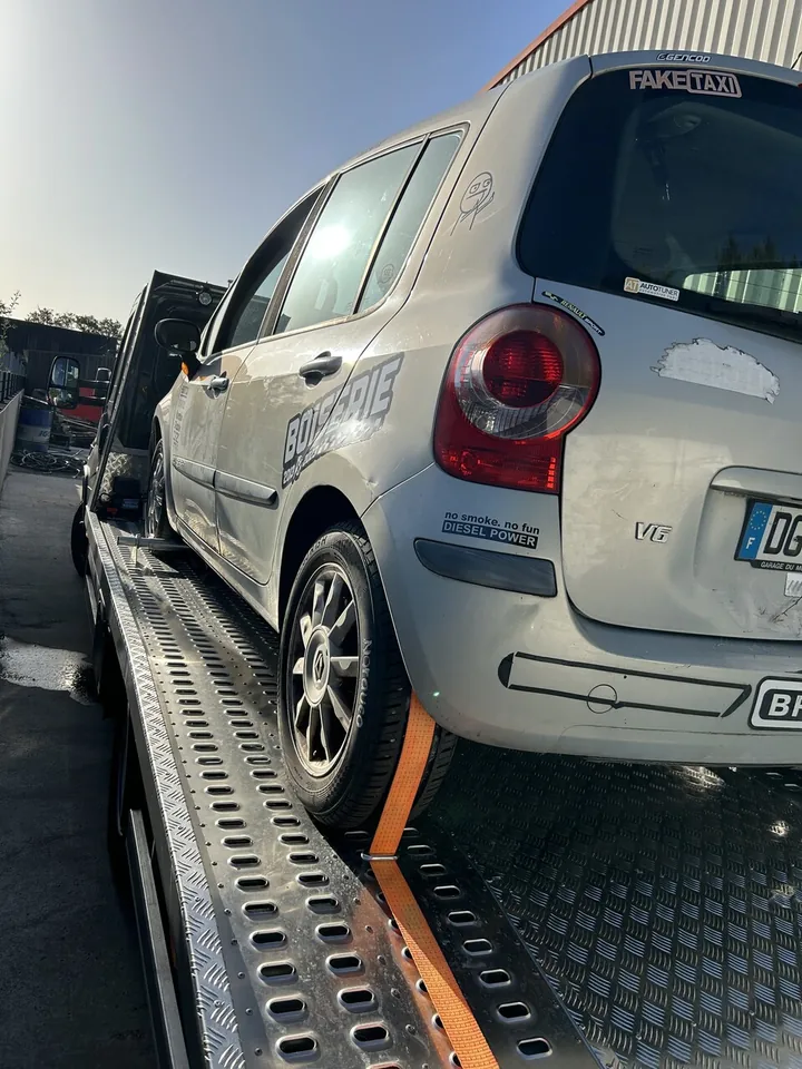 Voiture compacte claire sur un plateau perforé avec sangle passant sur une roue.