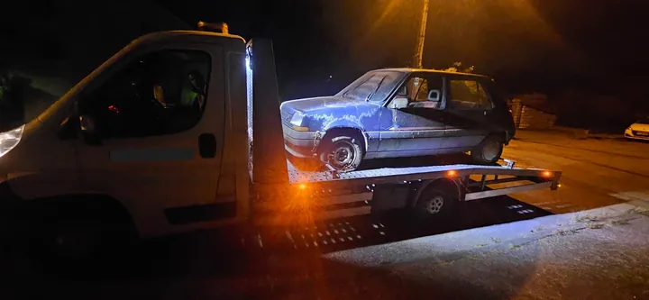 Voiture bleue chargée sur un camion plateau éclairé dans la nuit.