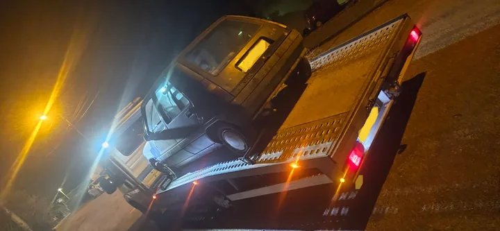 Voiture sombre sur un plateau métallique avec éclairages allumés la nuit.