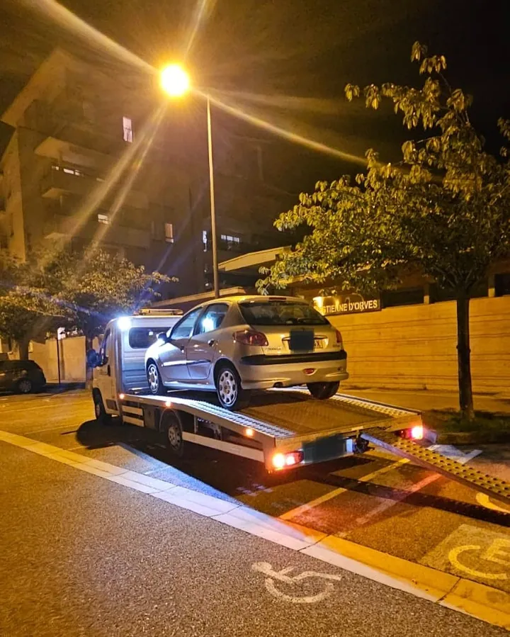 Voiture grise chargée sur un camion plateau sous un lampadaire.
