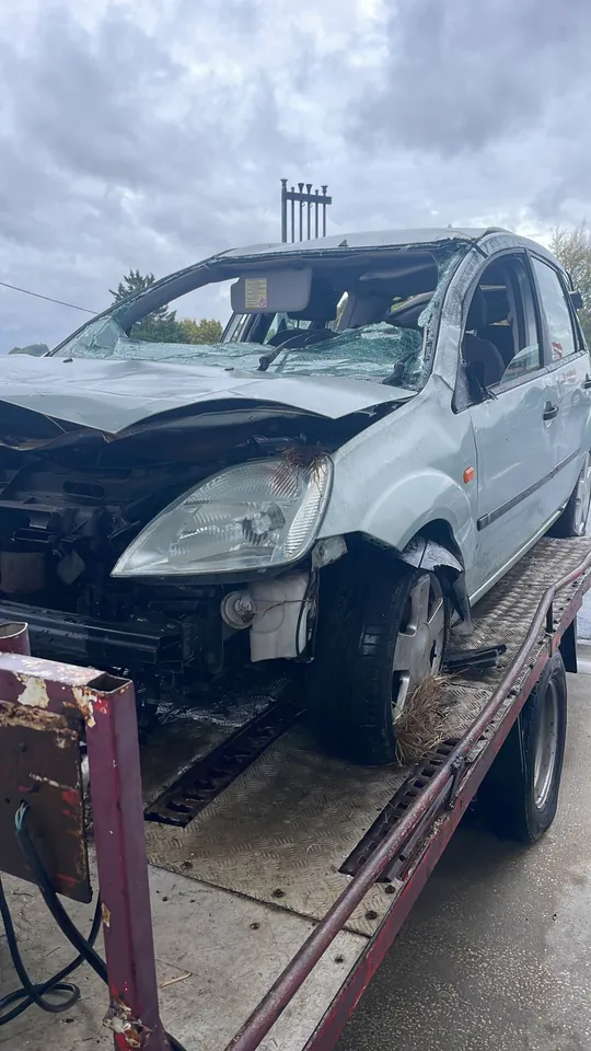 Voiture claire au capot déformé et au pare-chocs avant absent sur un plateau.