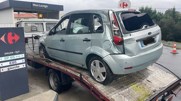 Voiture claire présentant des dégâts importants à l’arrière, installée sur un camion plateau.