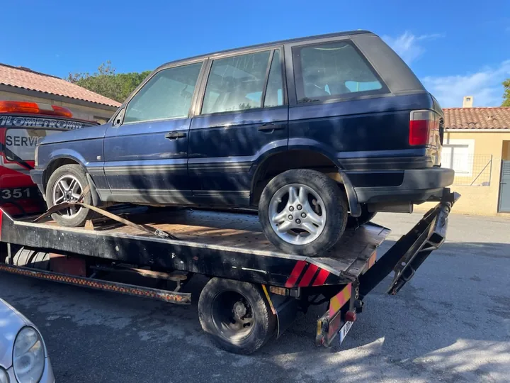 Véhicule bleu à carrosserie haute installé sur un camion plateau sombre.