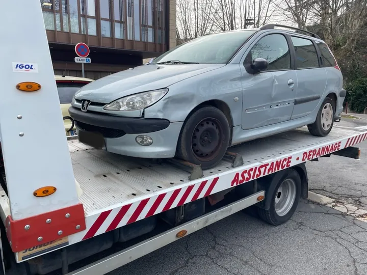 Voiture grise à cinq portes sur le plateau blanc d’une dépanneuse.