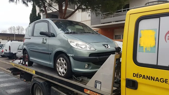 Petite voiture de couleur sombre sur un plateau à proximité d’un véhicule de dépannage.