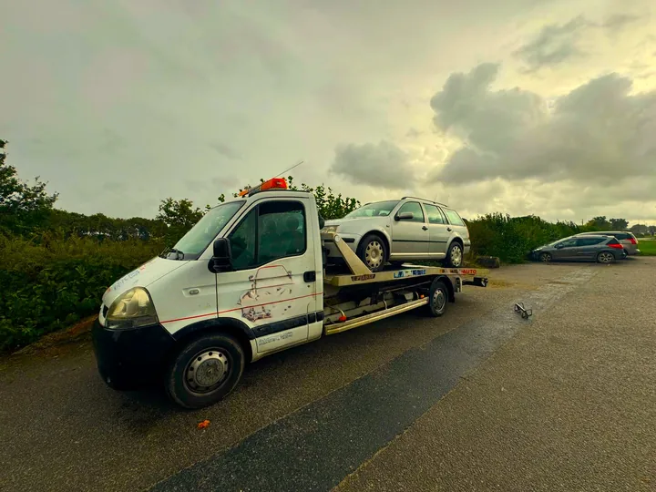 Camion blanc transportant une voiture claire sur une route dégagée.