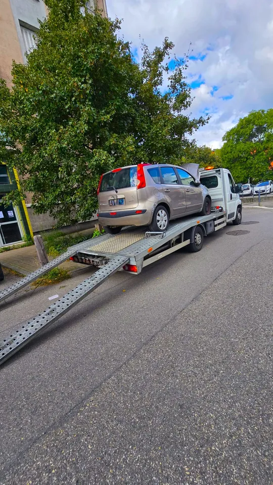 Voiture claire sur un plateau avec deux rampes métalliques abaissées vers la chaussée.
