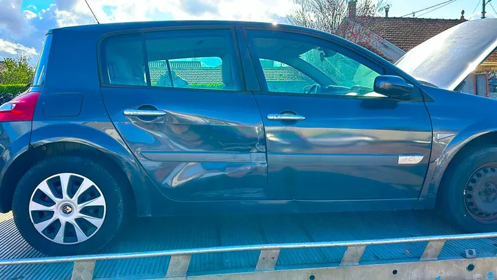 Voiture bleue présentant un enfoncement visible sur les portes latérales, installée sur un plateau.