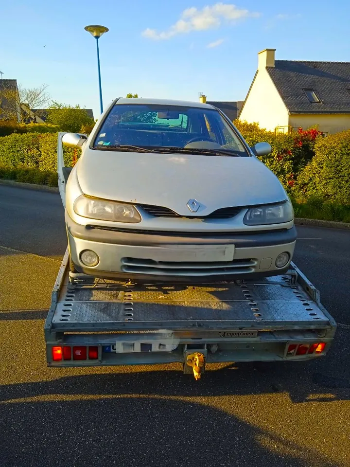 Petite voiture claire installée de face sur le plateau d’un camion.