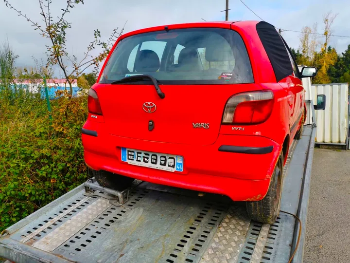 Citadine rouge chargée sur le plateau métallique perforé d’un camion.