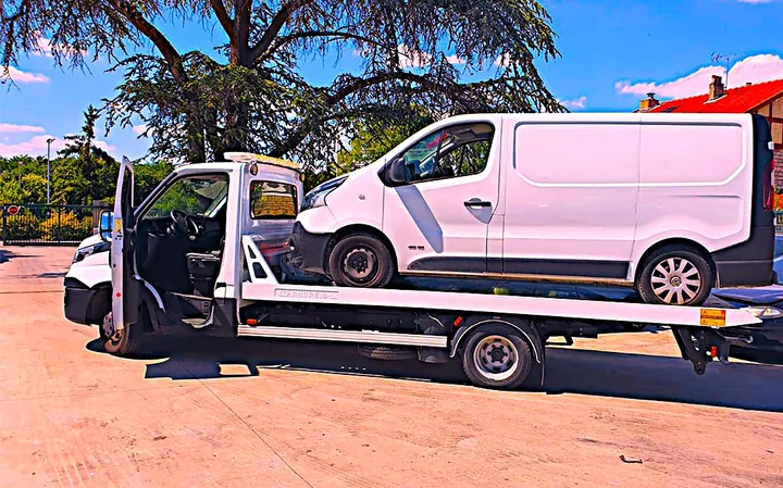 Fourgon blanc sur un camion plateau sombre avec une personne près de la cabine.