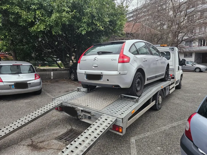 Voiture claire sur un camion plateau avec deux rampes déployées dans une rue.
