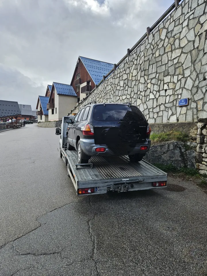 Voiture sombre sur un camion plateau stationné le long d’un mur dans une rue.