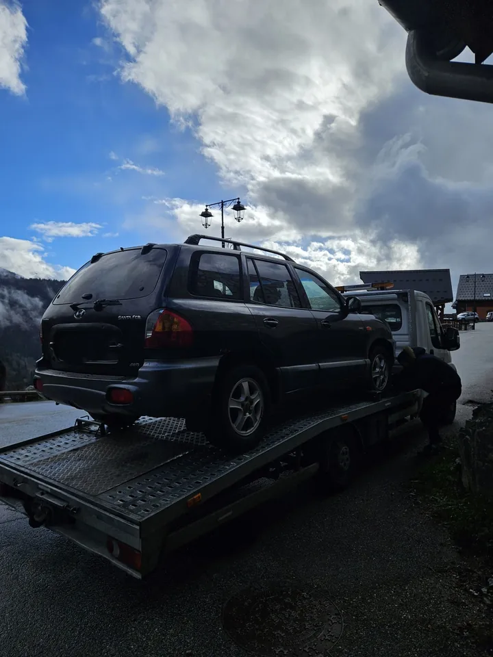 Véhicule familial sombre à carrosserie allongée sur le plateau d’un camion.