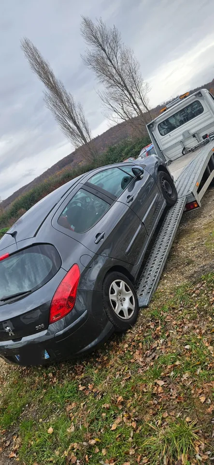 Voiture sombre vue de l’arrière près d’un plateau métallique et d’une zone herbeuse.