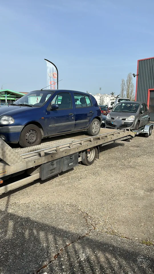 Voiture sombre sur un camion plateau et seconde voiture grise sur une remorque attelée.