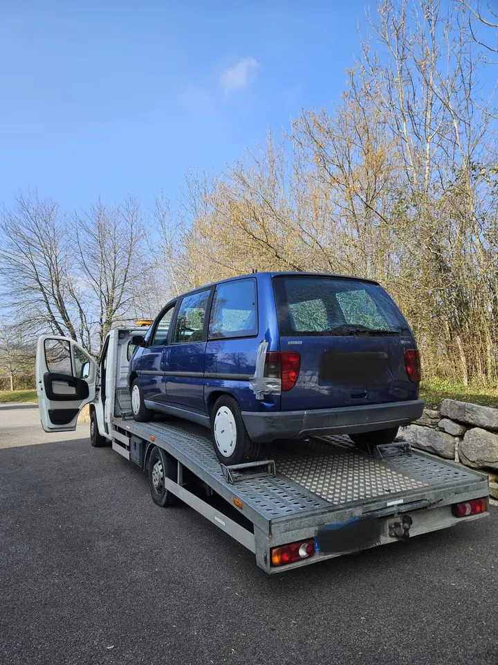 Voiture bleue à carrosserie haute photographiée de l’arrière sur un camion plateau.