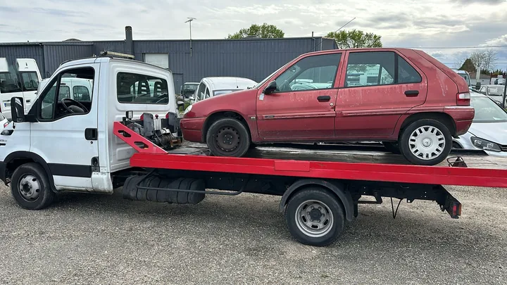 Citadine rouge à cinq portes installée sur le plateau d’un camion blanc.