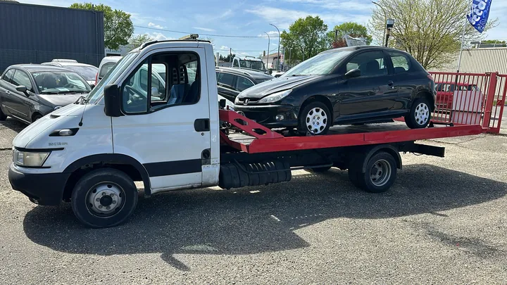 Camion blanc transportant une voiture sombre sur son plateau.