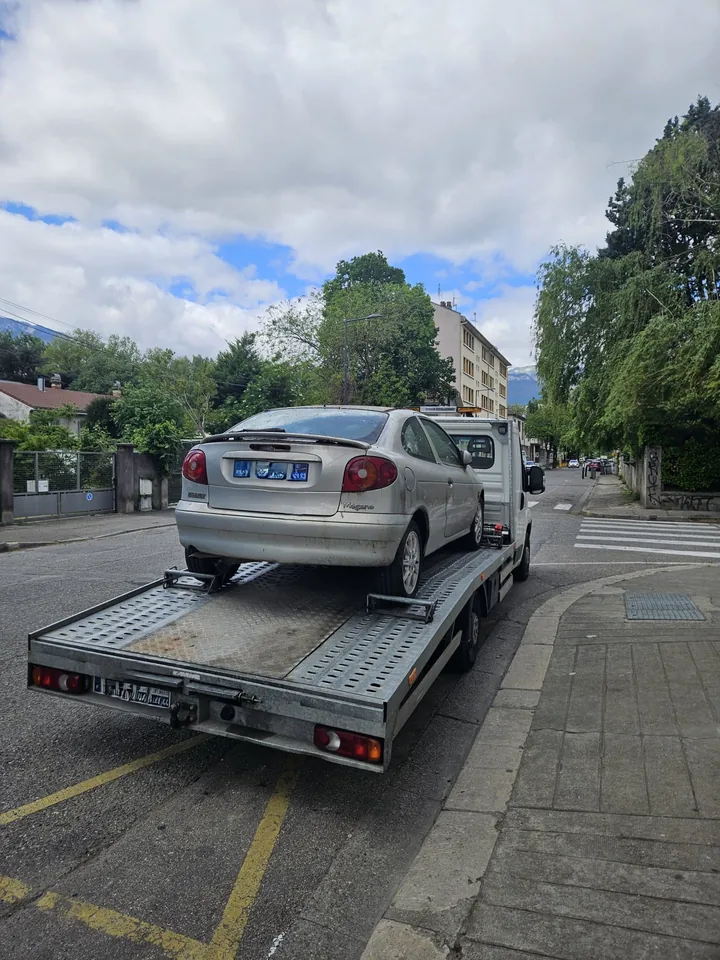 Voiture claire sur un camion plateau garé le long des stationnements d’une rue.