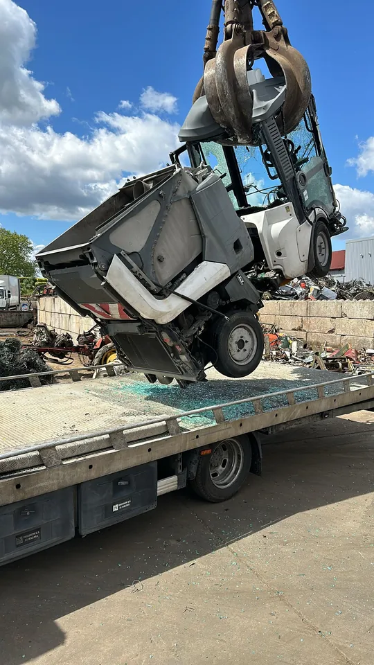 Balayeuse compacte suspendue à une pince de manutention au-dessus d’un plateau.