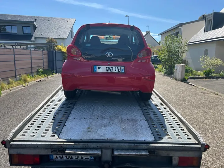 Arrière d’une Toyota Aygo rouge sur le plateau d’une dépanneuse.