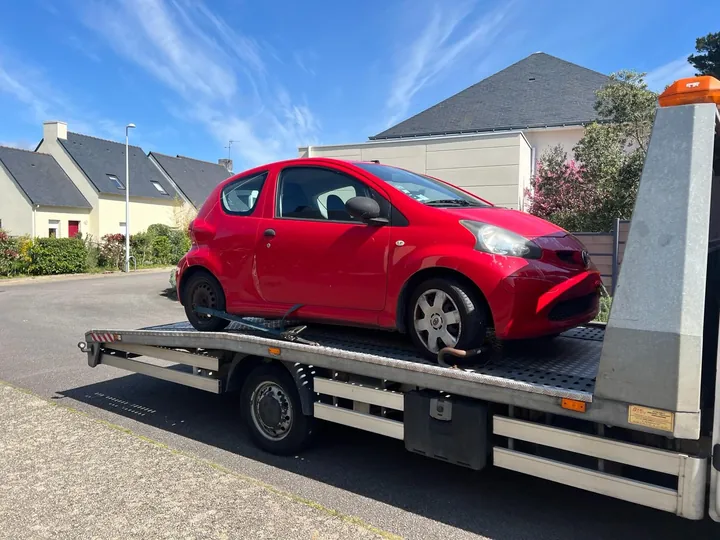 Citadine rouge chargée de profil sur une dépanneuse blanche.