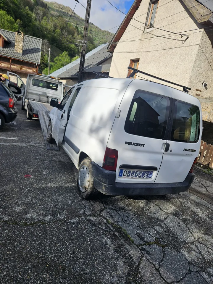 Fourgonnette blanche alignée devant une dépanneuse entre des maisons.