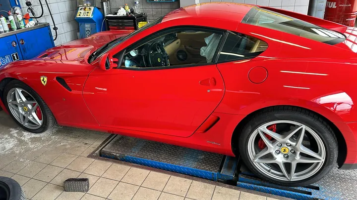 Coupé sportif rouge positionné sur les rails d’un équipement d’atelier.