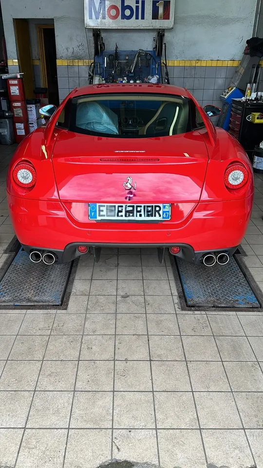 Arrière d’un coupé sportif rouge sur deux rails métalliques en atelier.