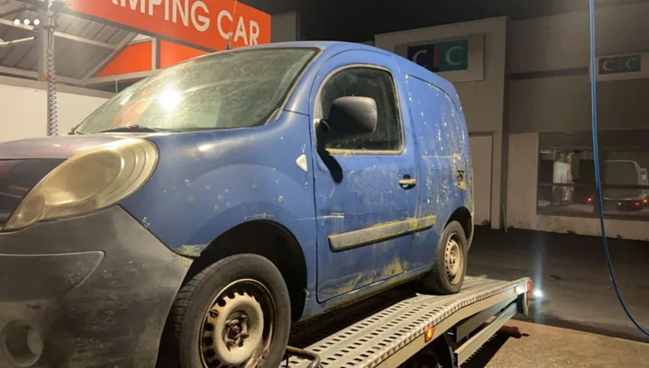 Fourgonnette bleue à carrosserie marquée sur un plateau, dans un local.
