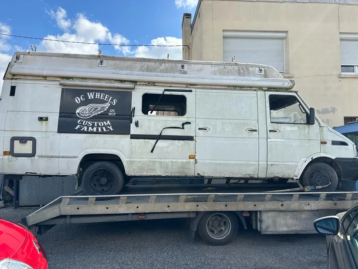 Ancien fourgon blanc à toit haut chargé sur une dépanneuse.